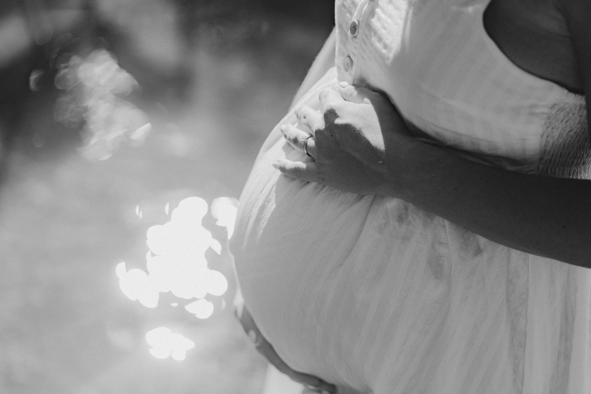 Paar hält gemeinsam den Babybauch im Gegenlicht, schwarz-weiß — Babybauchfotografie München