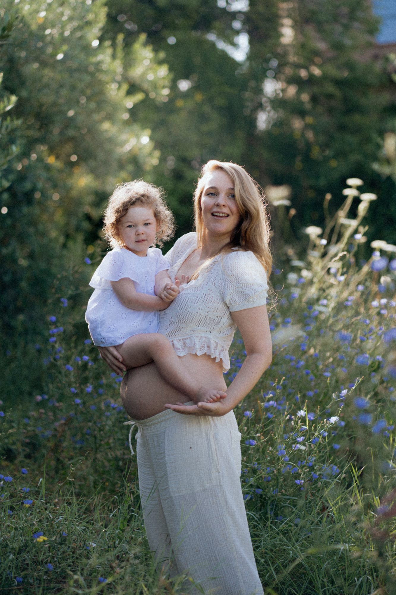 Schwangere Mutter mit Kind auf dem Arm in Wildblumen — Familienfotografie