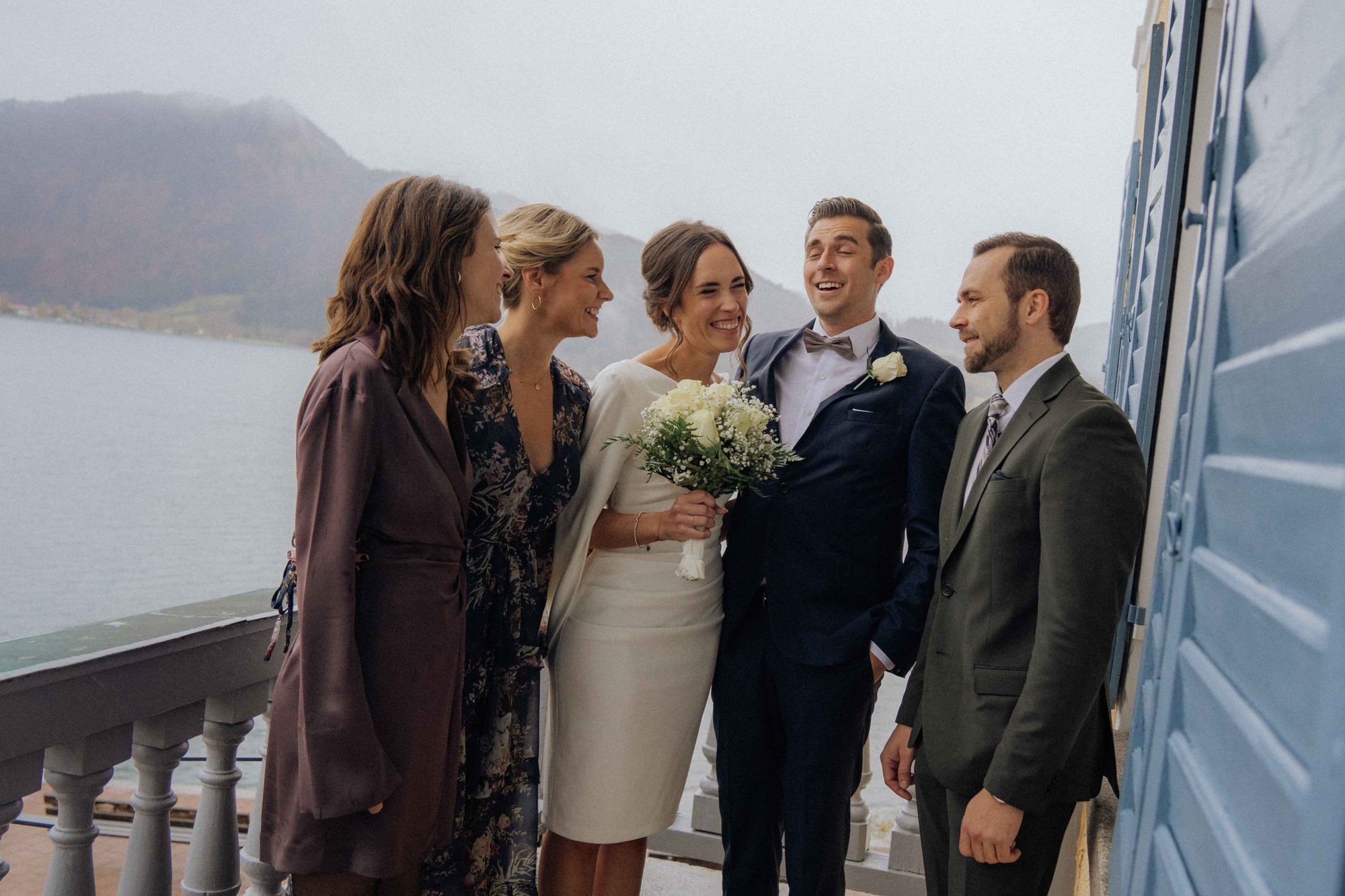 Lachende Hochzeitsgesellschaft auf dem Balkon am See