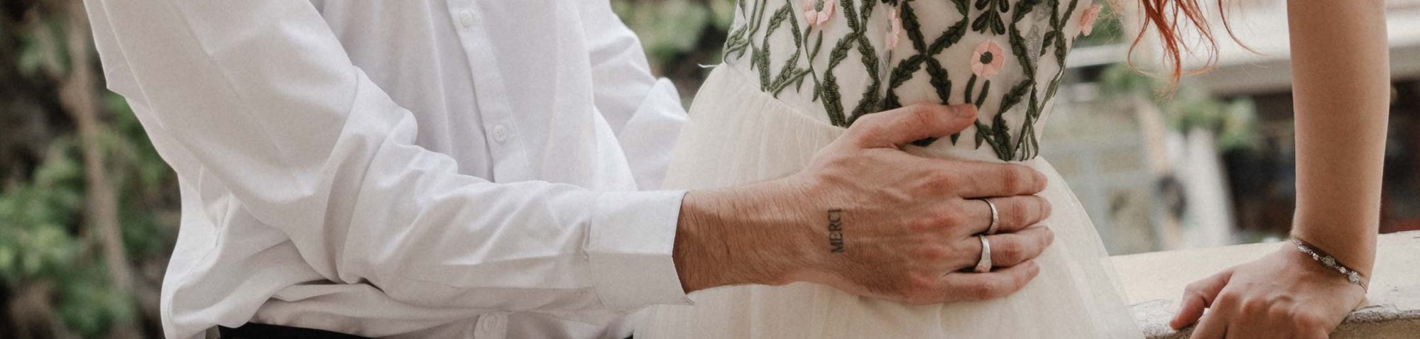 Hände-Detail mit Eheringen und MERCI-Tattoo